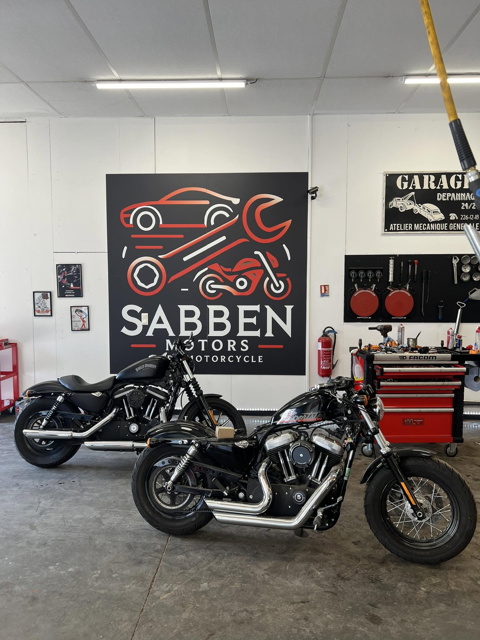 Deux motos Harley-Davidson garées devant le logo Sabben Motors dans l'atelier