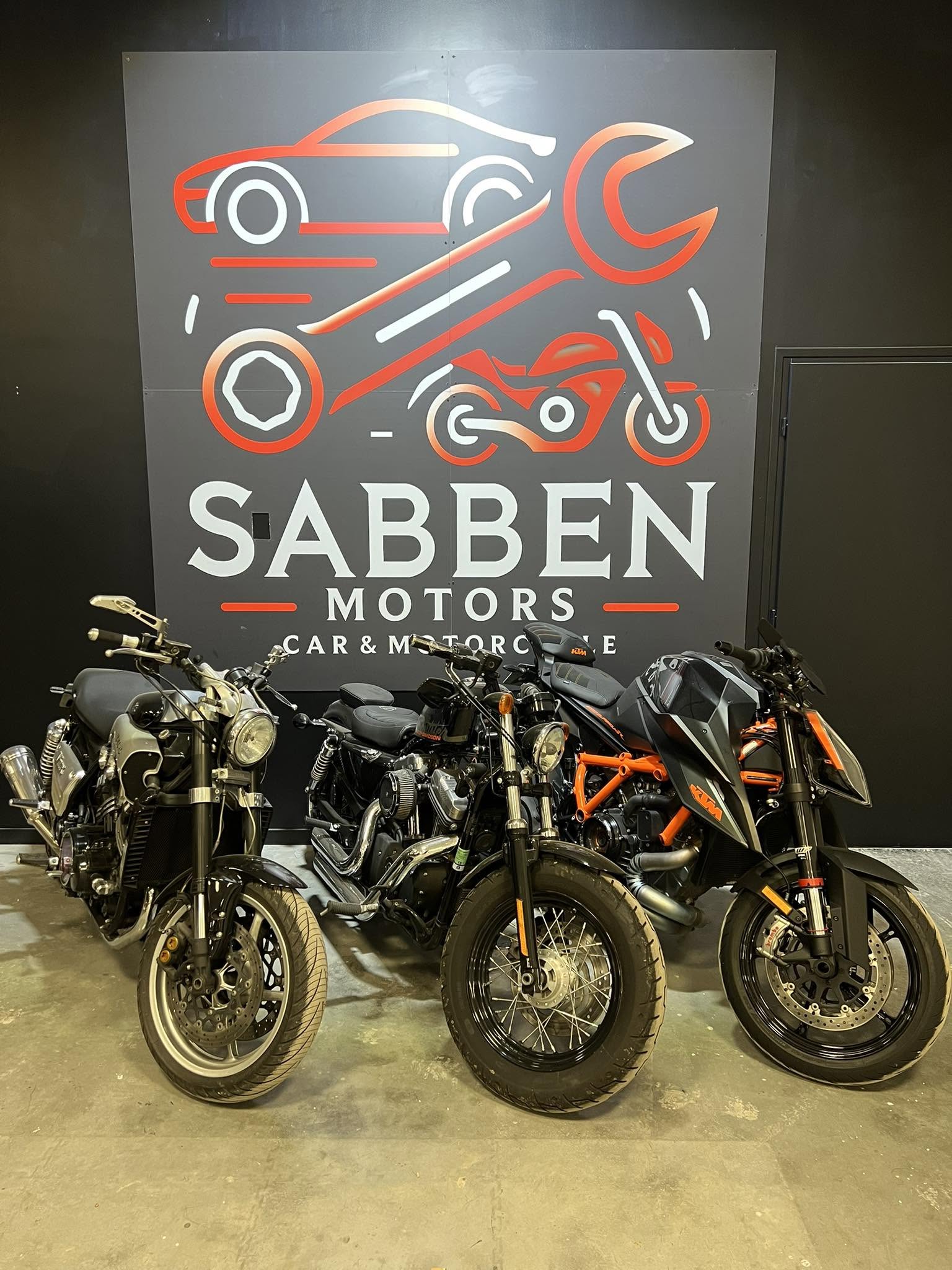 Trois motos alignées devant le logo Sabben Motors dans l'atelier